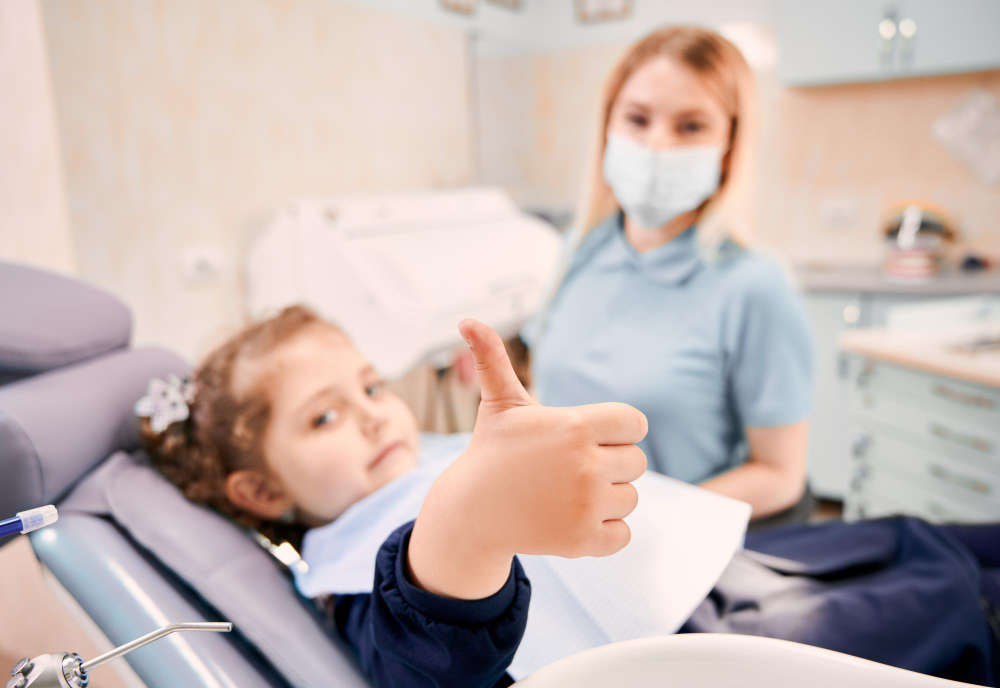 Female dentist and cute little girl giving thumbs up