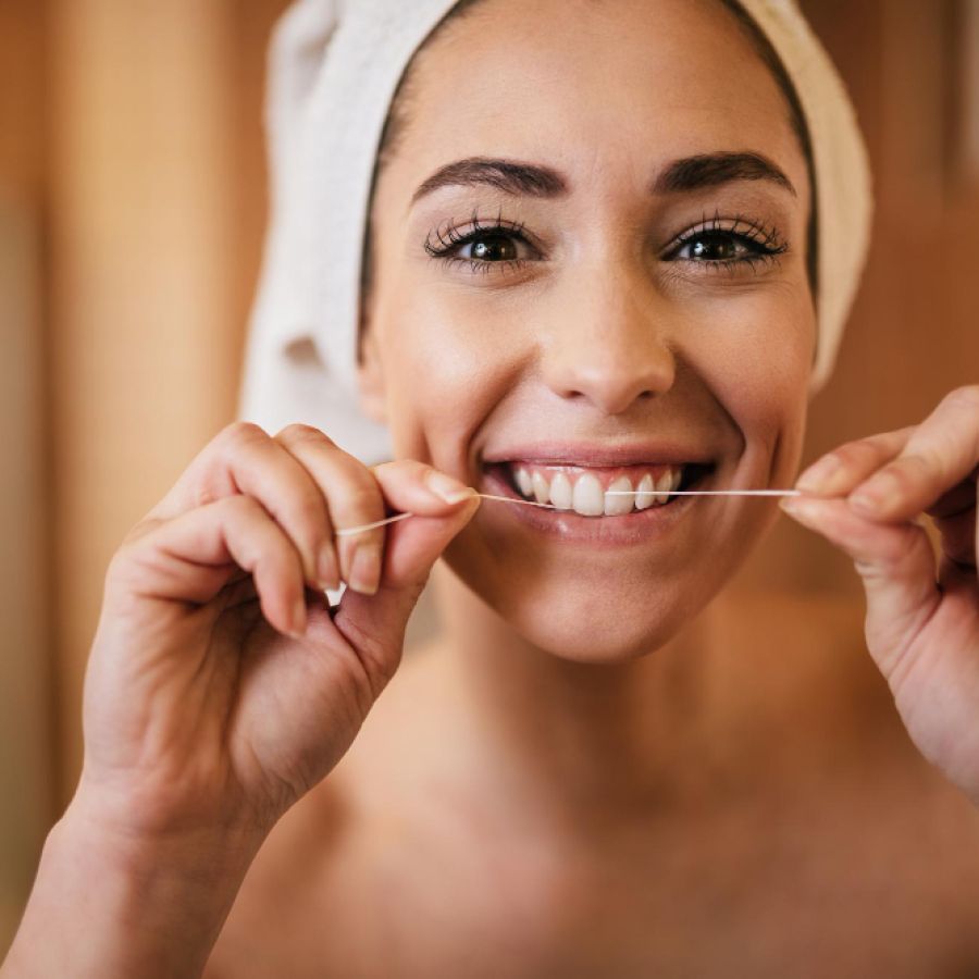 Woman with a white towel on her head is flossing Infront of a mirror and smiling