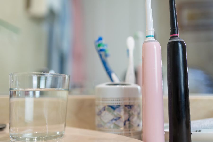 two electric toothbrushes on a sink with a glass of water depicting good oral hygiene