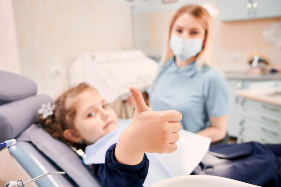 Female dentist and cute little girl giving thumbs up