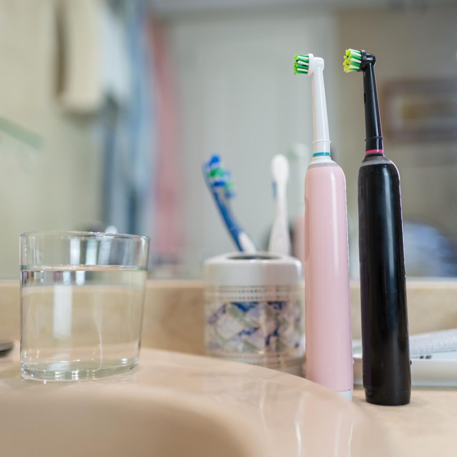 two electric toothbrushes on a sink with a glass of water depicting good oral hygiene